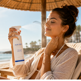 Femme appliquant Aloe First™ Forever Living sous un parasol sur une plage ensoleillée pour une sensation de fraîcheur et d'hydratation