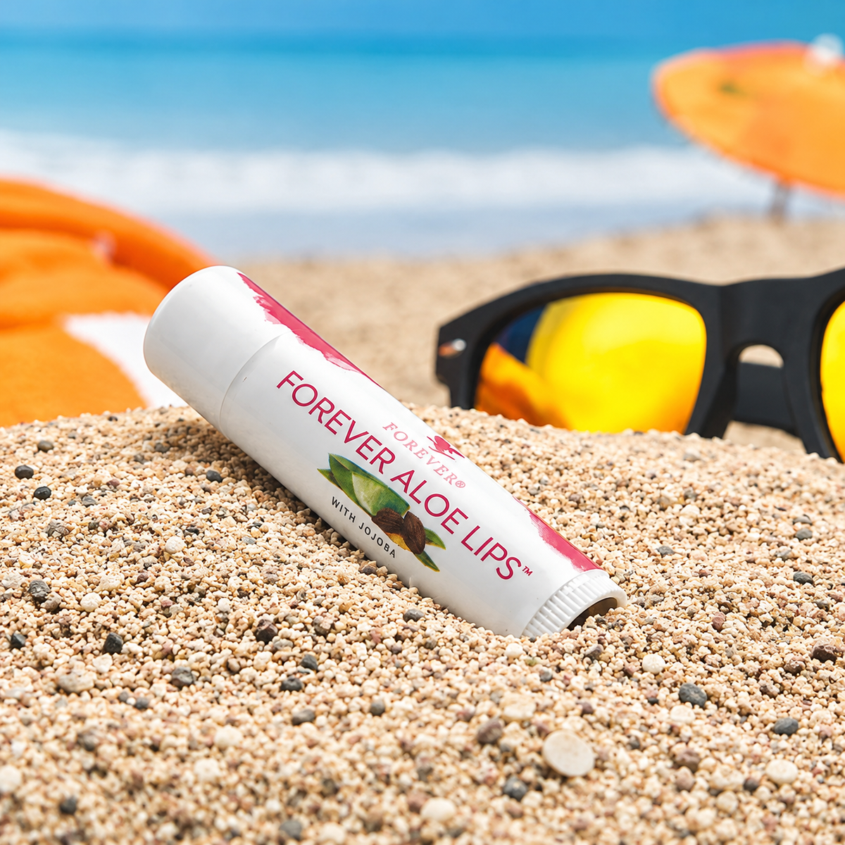 Baume à lèvres Forever Aloe Lips à l’Aloe vera et au jojoba présenté sur le sable à la plage