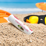 Baume à lèvres Forever Aloe Lips à l’Aloe vera et au jojoba présenté sur le sable à la plage
