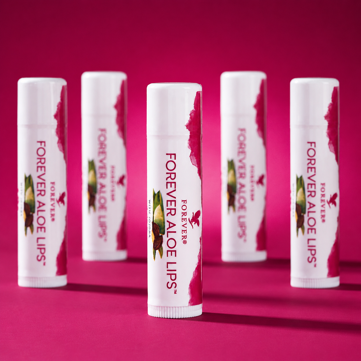 Plusieurs baumes à lèvres Forever Aloe Lips à l’Aloe vera et au jojoba sur fond rose