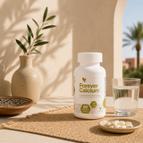 Flacon Forever Calcium™ présenté sur une table avec un verre d'eau et des comprimés dans une ambiance naturelle et épurée.